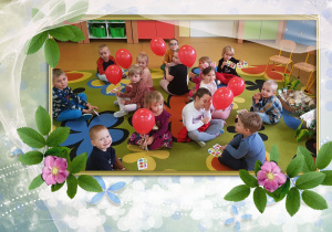 Dzieci siedzą na dywanie. Dziewczynki trzymają czerwone balony.